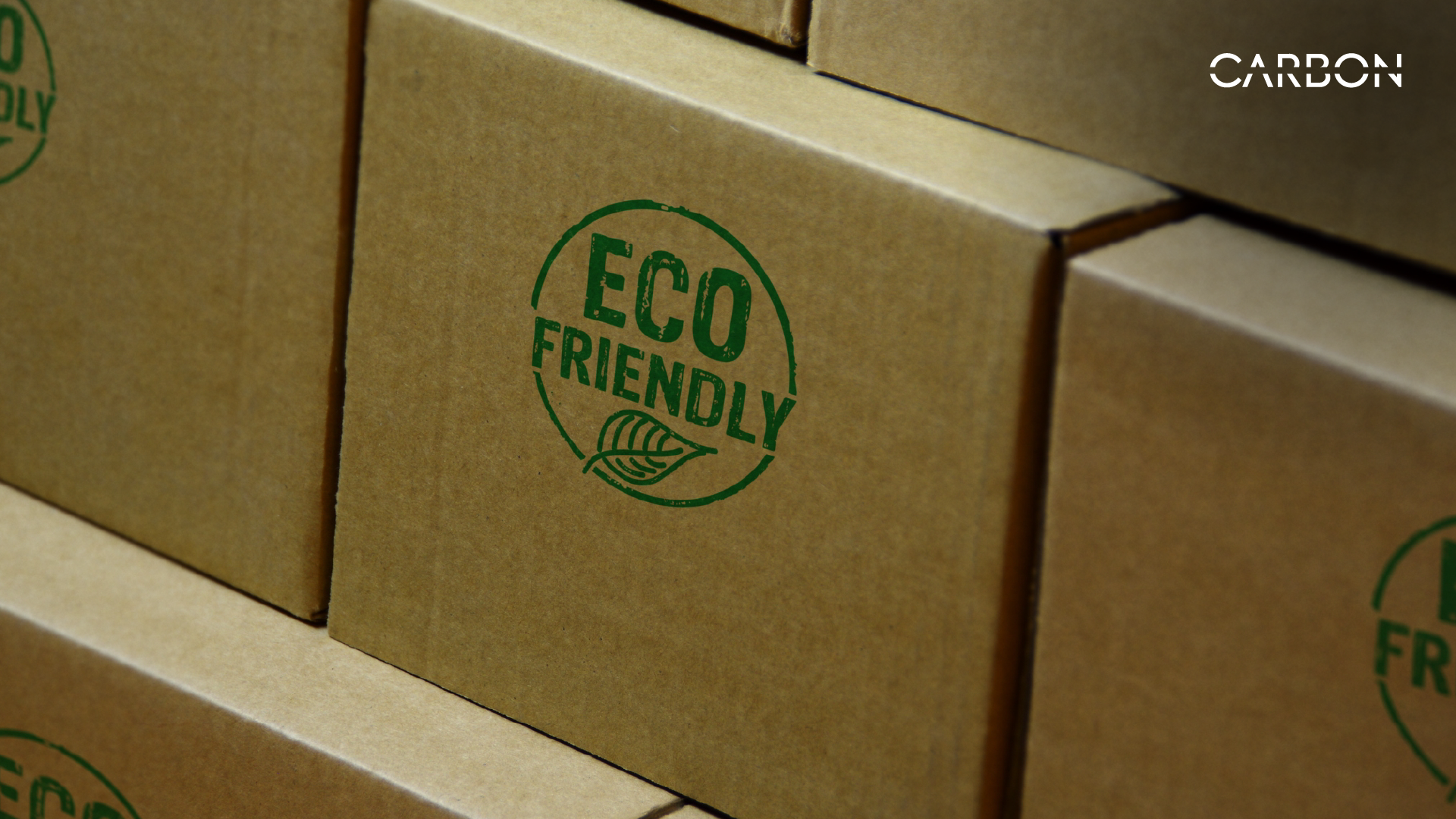 Close-up of stacked cardboard boxes with a green "ECO FRIENDLY" stamp printed on them. The boxes symbolize sustainable packaging and the push for bio-based, environmentally friendly materials.